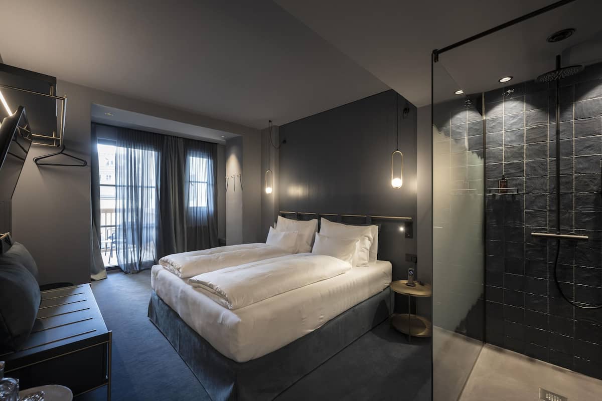 Habitació d'hotel moderna amb un llit gran, taules de nit, escriptori i zona de dutxa.