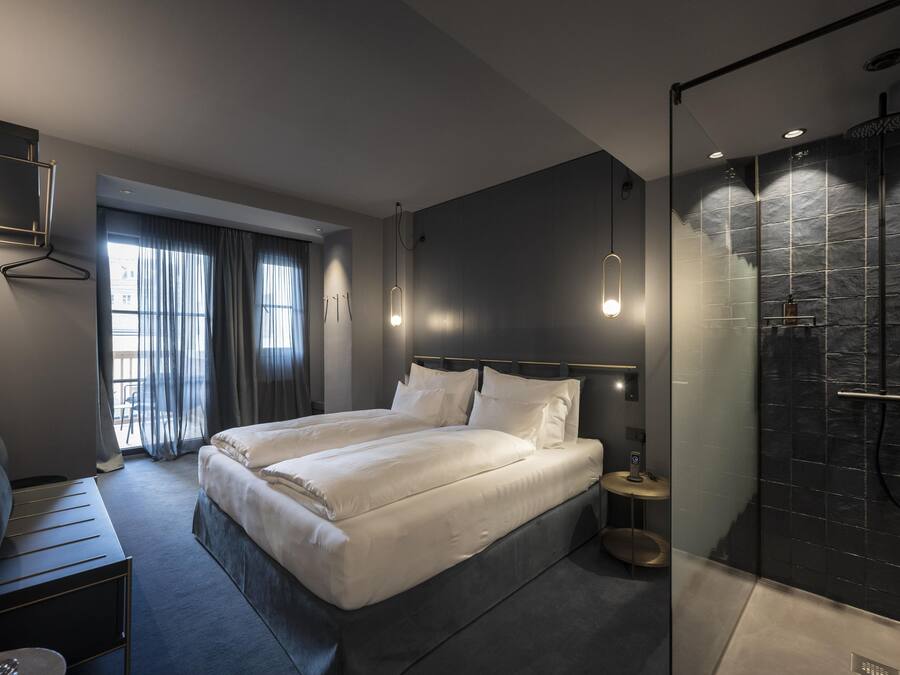 Una habitación de hotel moderna con una cama grande, mesitas de noche, un escritorio y zona de ducha.