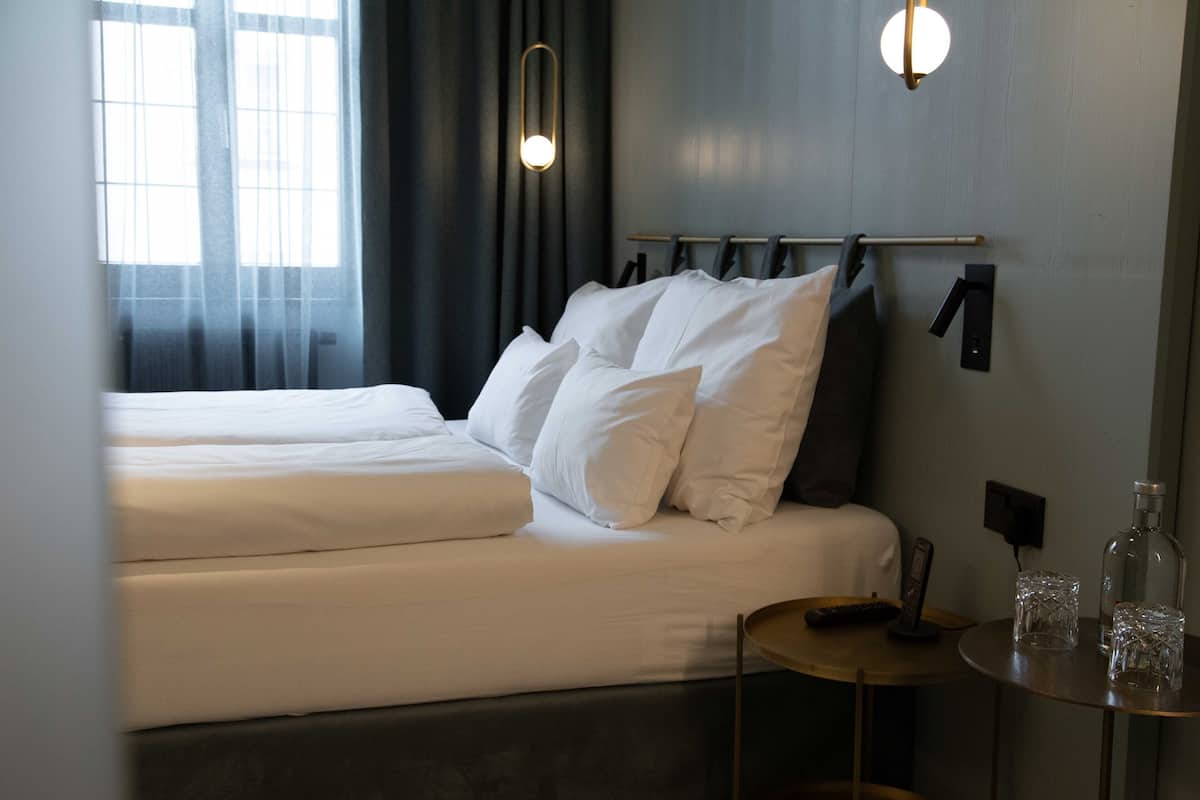 Habitació d'hotel amb dos llits, una tauleta de nit amb un comandament a distància i una taula petita amb dos vasos.