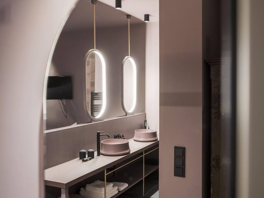 A modern bathroom with a vanity, two illuminated mirrors, a sink, and a television mounted on the wall.
