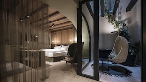 A modern bedroom with a bed, a chair, and a hanging plant.