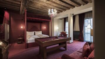 Een kamer met een pooltafel, een bed met hemelbed, een kroonluchter en uitzicht op de stad door grote ramen.