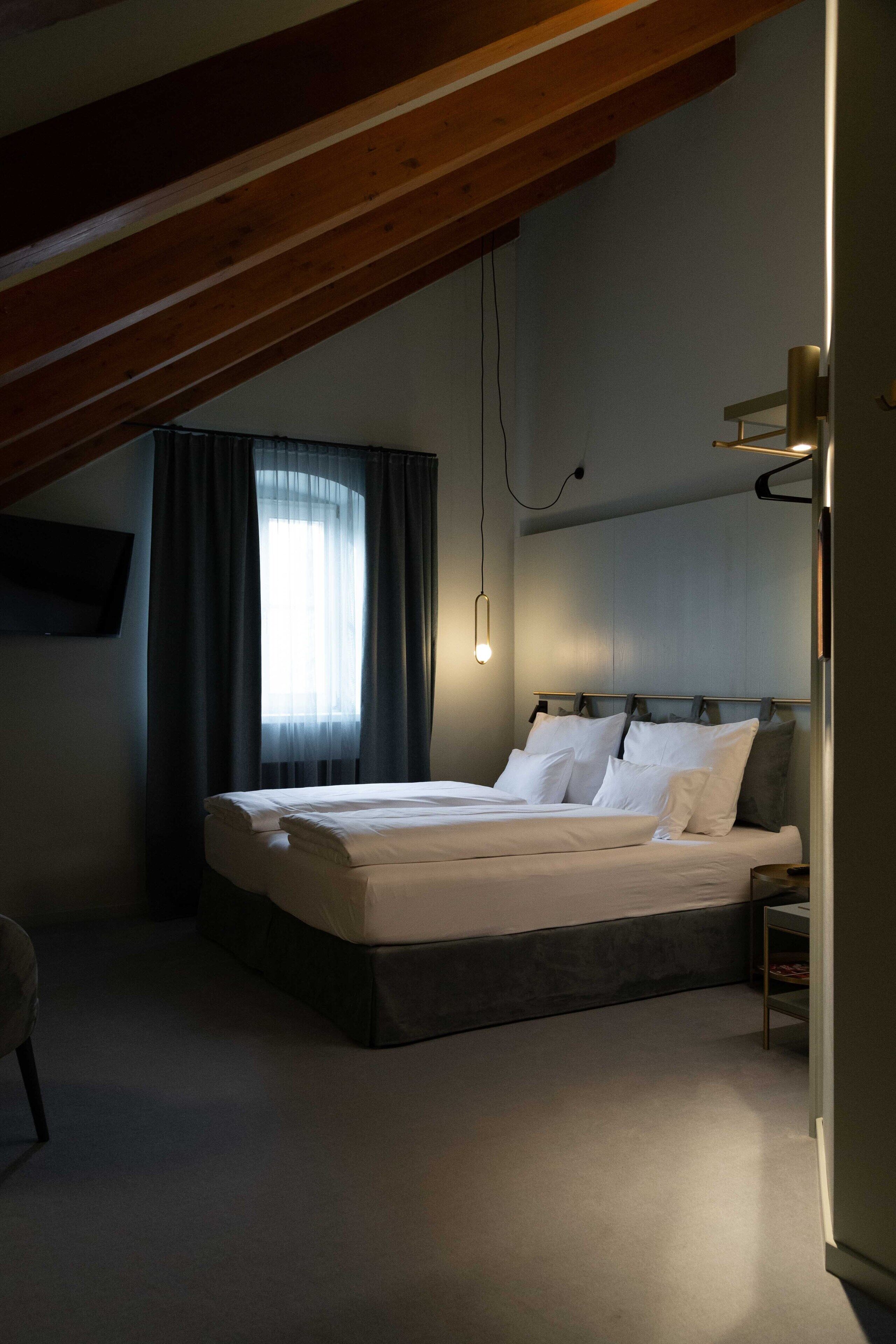 A bedroom with a bed, a bedside table, a wall-mounted TV, and a window with curtains.