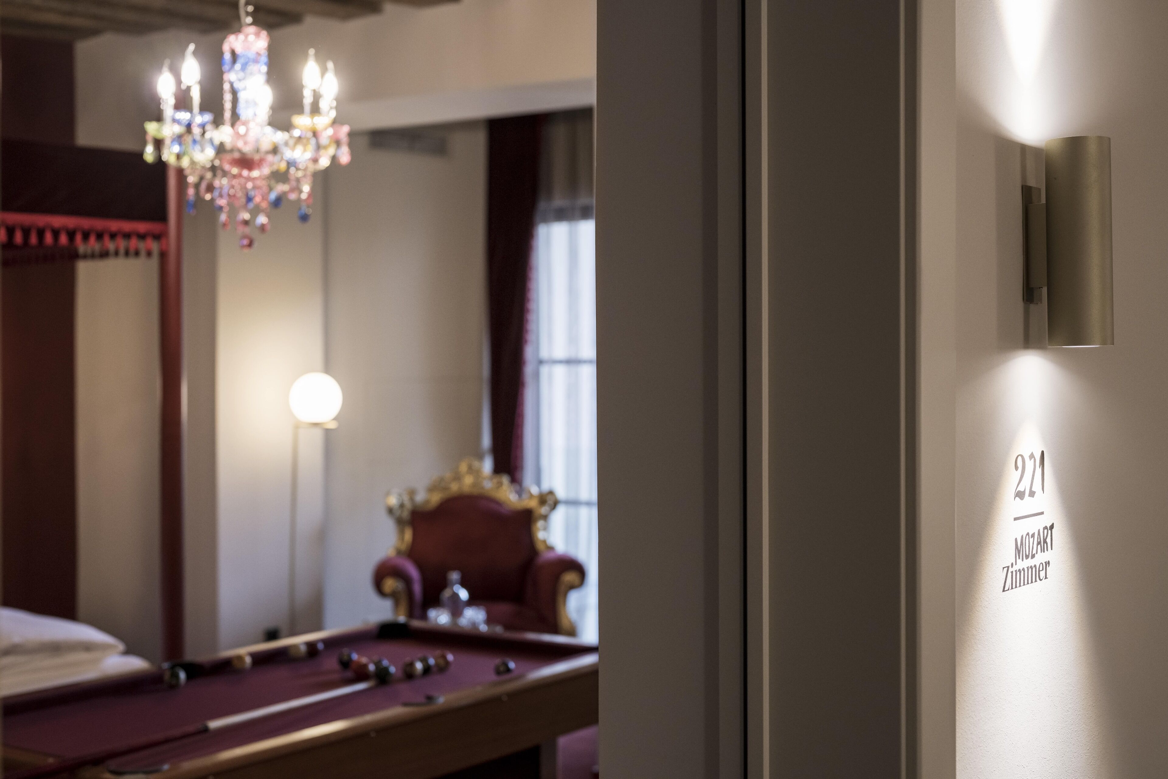 A pool table in a room with a chandelier and a wall-mounted light fixture.