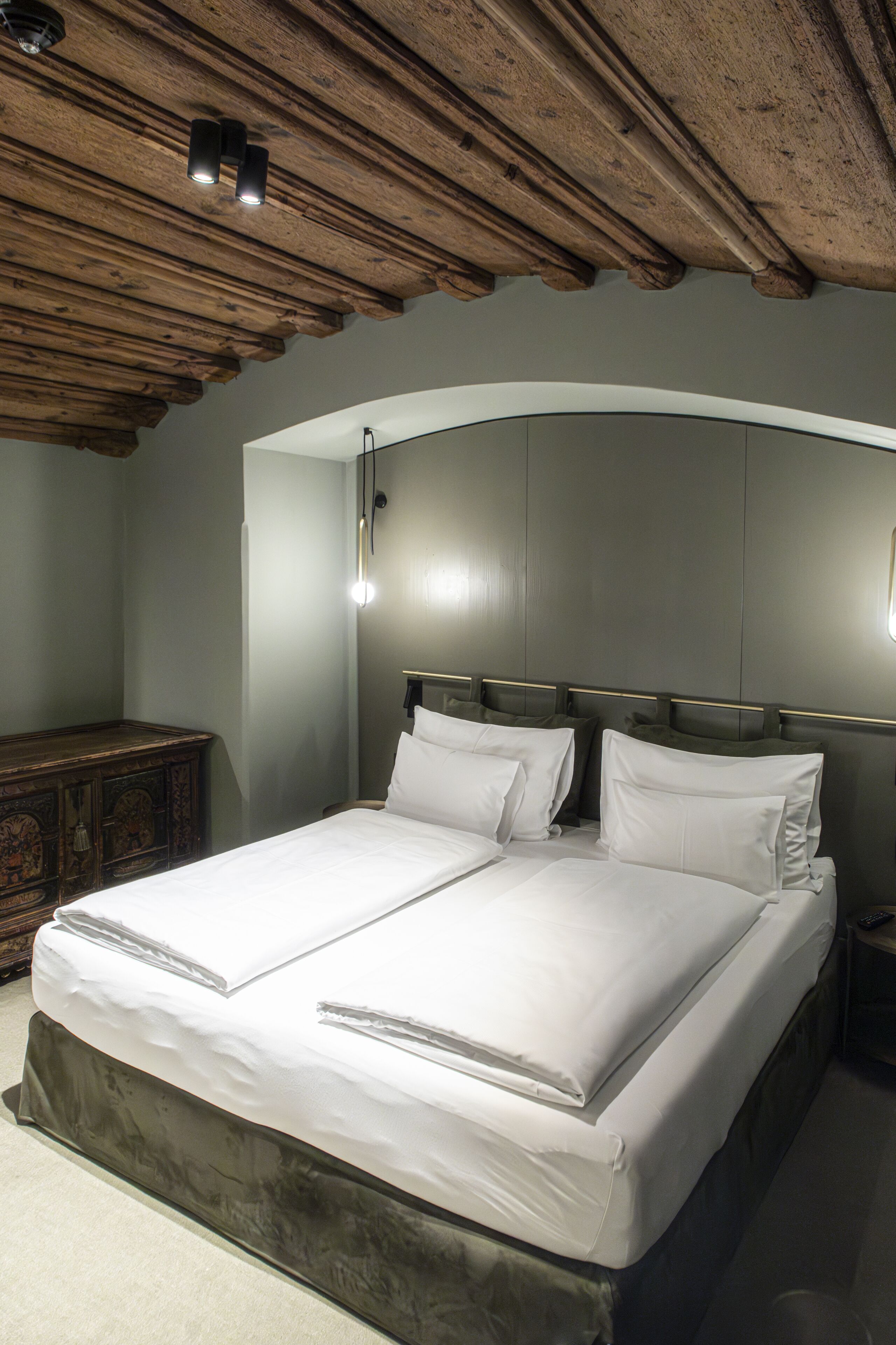 A double bed with white linens in a room with a wooden ceiling and a curved wall.
