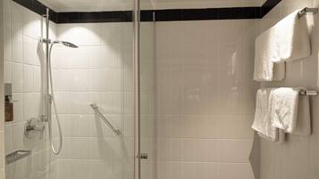 Un baño moderno con ducha envuelta en cristal, azulejos blancos y dos toallas colgadas en un perchero.