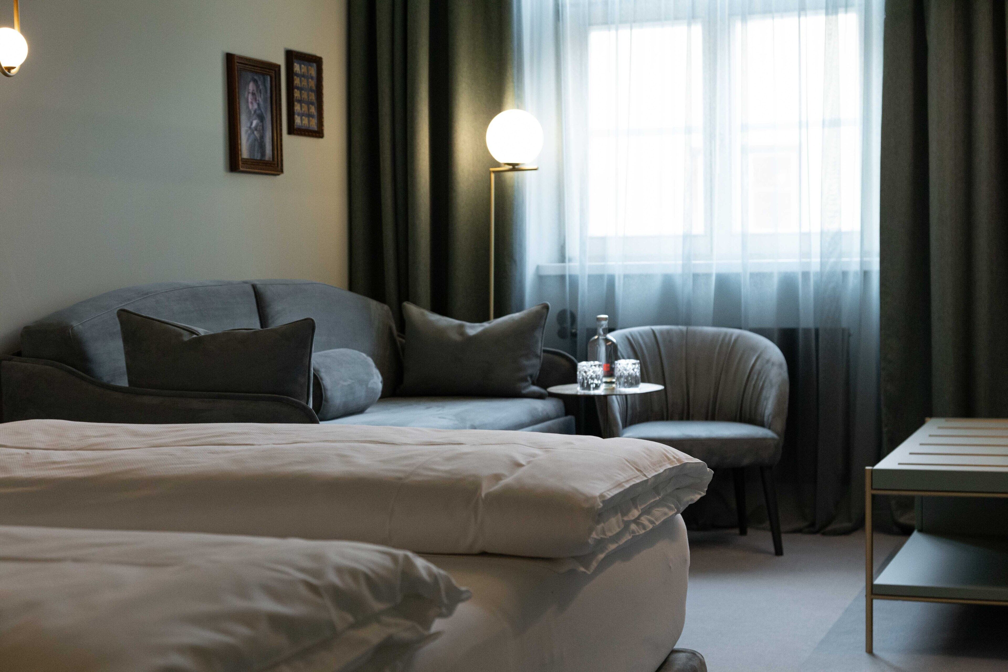 A hotel room with a large bed, a sofa, a chair, a small table, and a floor lamp.