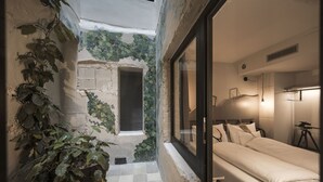 A narrow corridor with a checkered floor leading to a doorway, a bed with white bedding, and a tripod-mounted camera on the right.