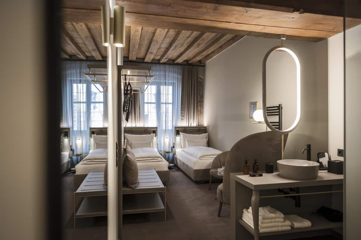 Habitació d'hotel amb dos llits, zona de seients, un gran mirall i un bany amb rentapelats i porta tovalloles.