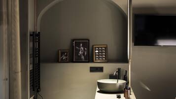 Un baño moderno con un lavamanos grande, un espejo y un televisor montado en la pared.