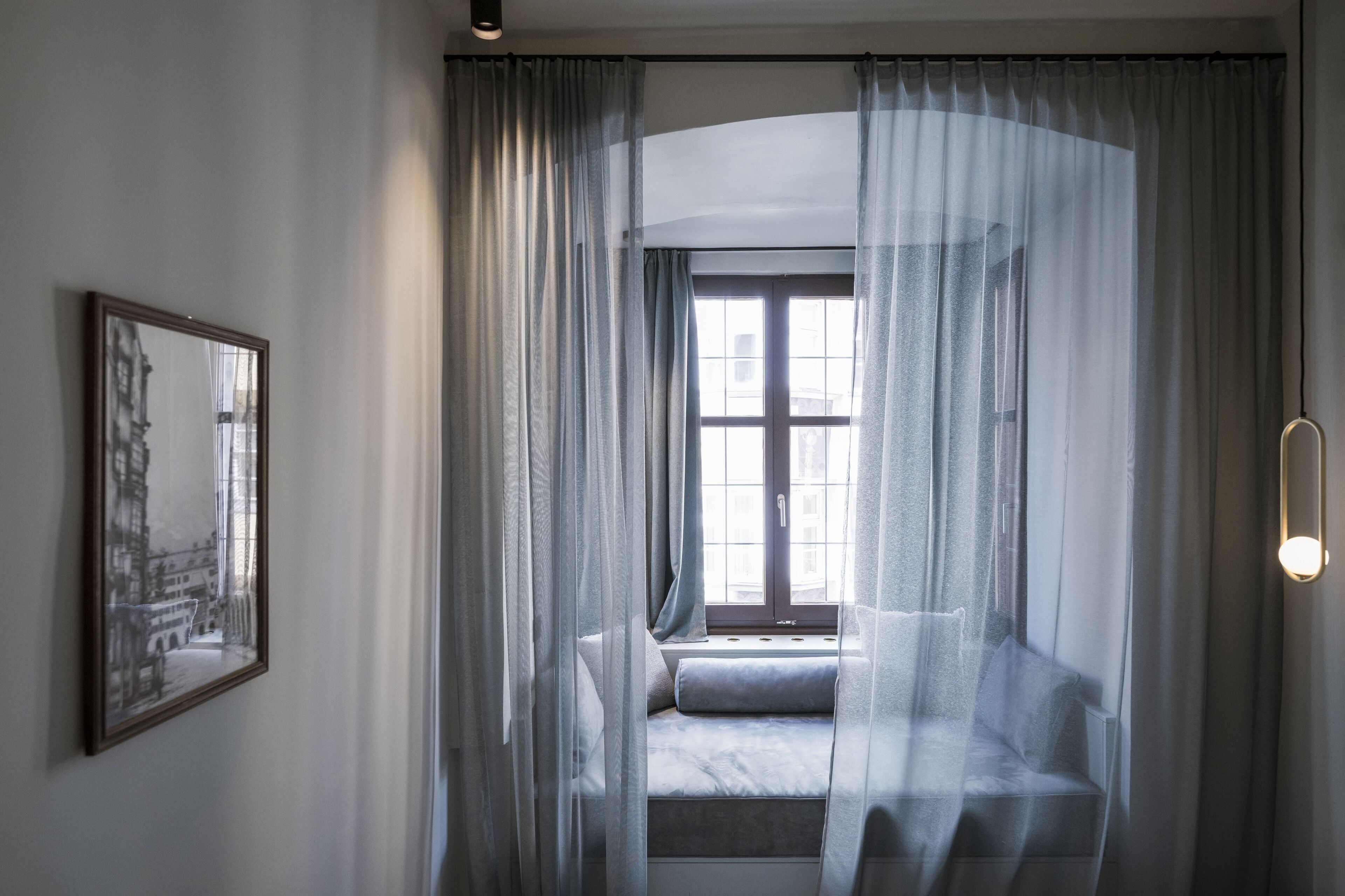 A room with a window seat, sheer curtains, and a framed picture on the wall.