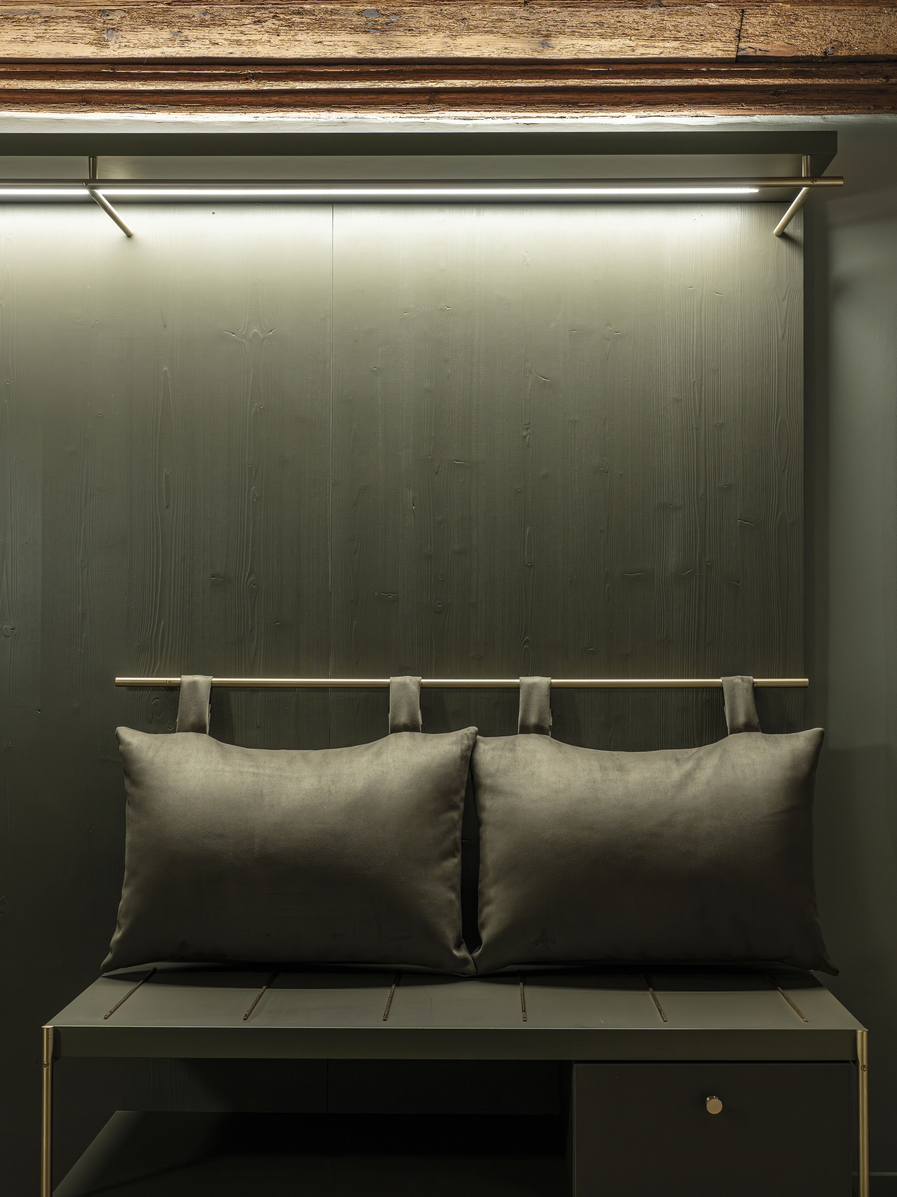 A bed with two pillows and a wooden headboard against a dark wall.