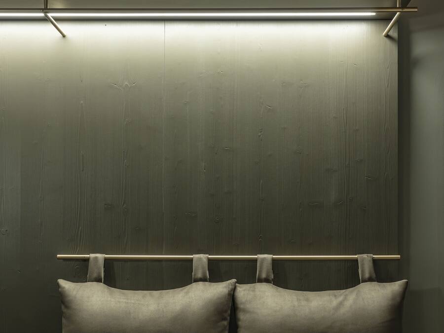 A bed with two pillows and a wooden headboard against a dark wall.