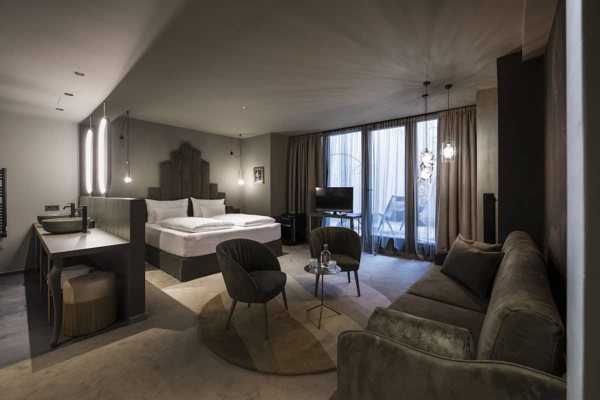 Una habitació d'hotel moderna amb un llit, un sofà, una taula de treball i una làmpada, i també una televisió.