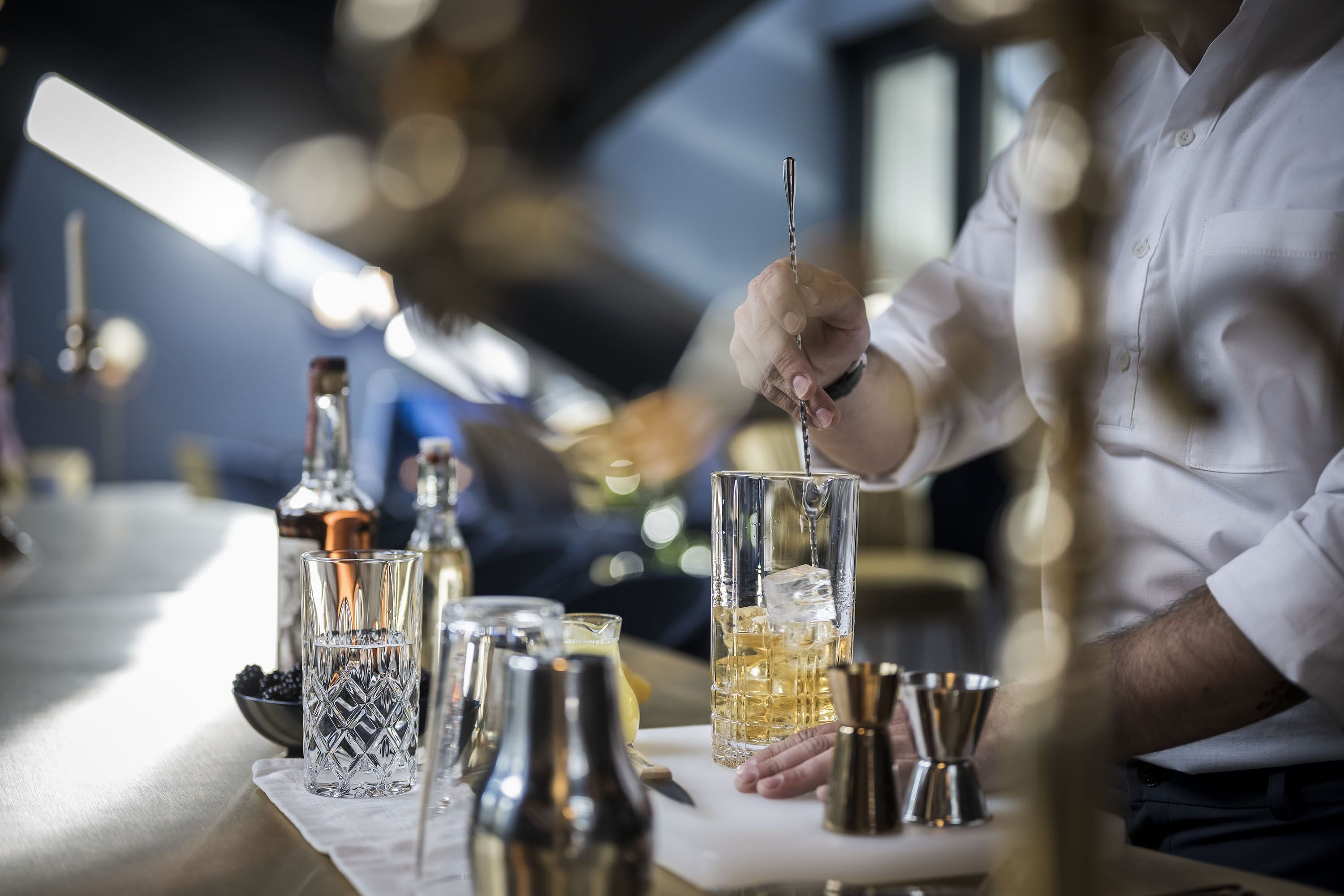 A bartender preparing a drink with a shaker and a tall glass.