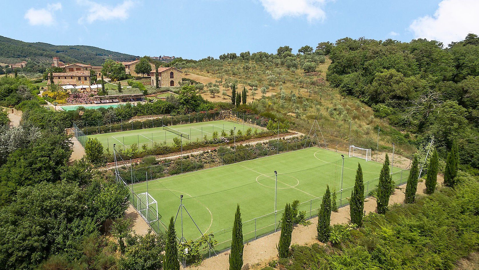 Un court de tennis entouré d’arbres et un bâtiment avec un toit rouge.