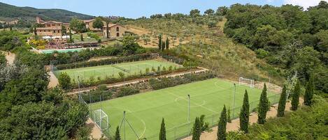 Un court de tennis entouré d’arbres et un bâtiment avec un toit rouge.