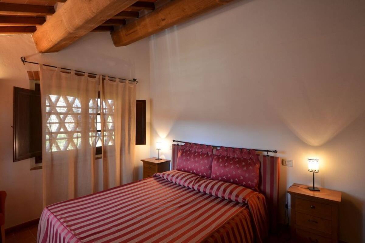 A bedroom with a bed, two bedside tables, a nightstand, a chair, and a window with curtains.