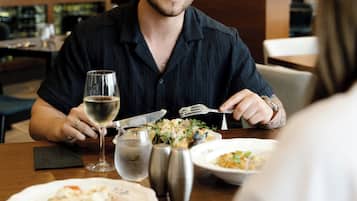 Una persona cenando en una mesa, con una copa de vino, un vaso de agua y saleros y pimenteros.