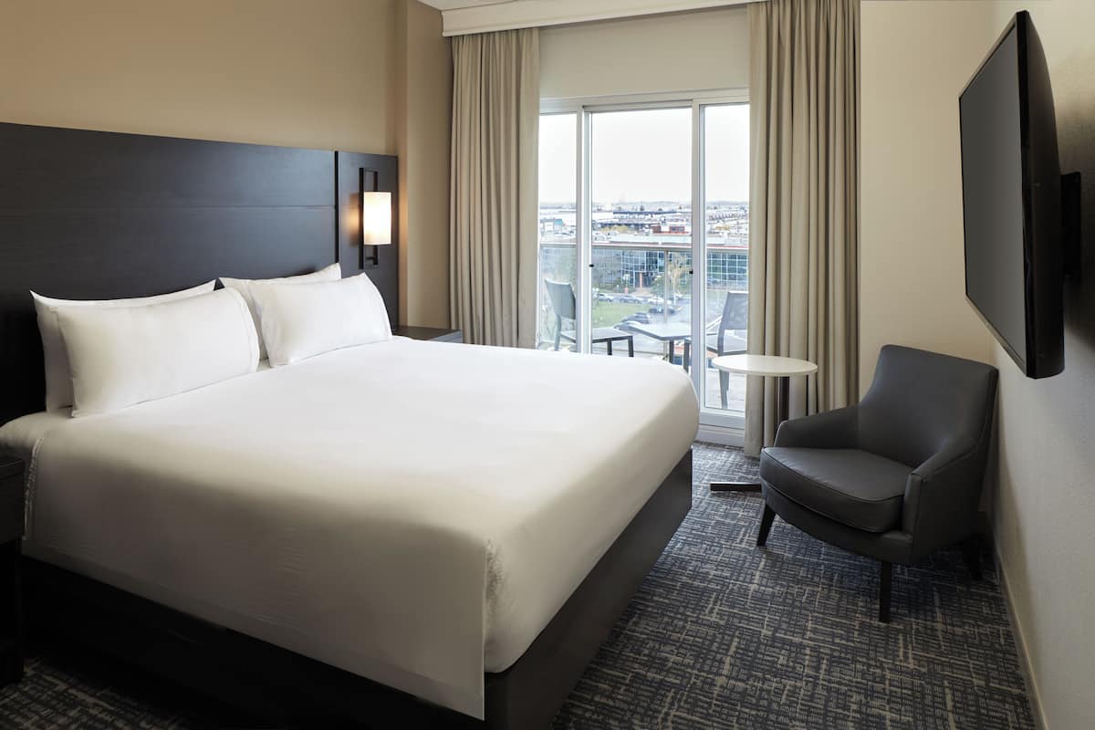 Een hotelkamer met een groot bed, een stoel, een televisie en uitzicht op de stad.