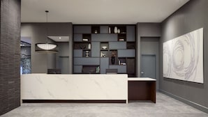 Een moderne receptie met een marmeren balie, een groot abstract schilderij en diverse decoratieve objecten op planken.