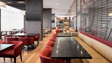Un restaurante moderno con mesas largas compartidas, sillas tapizadas en rojo y un gran adorno en la pared.