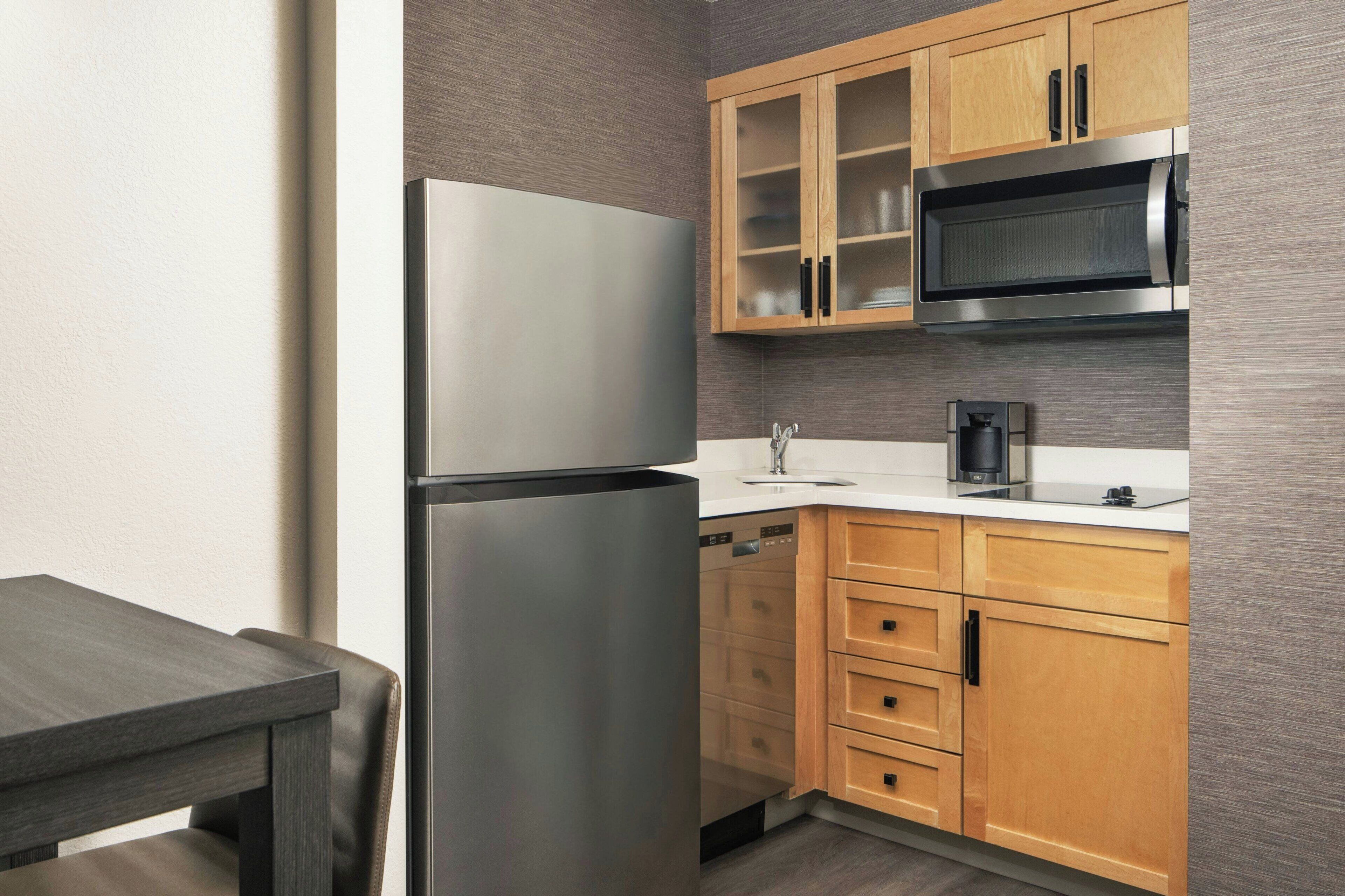 A compact kitchen with a stainless steel refrigerator, a microwave, and wooden cabinets.