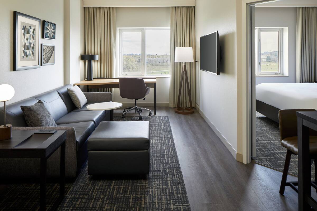 Een hotelkamer met een bank, voetenbankje, bureau, stoel, televisie en een bed.