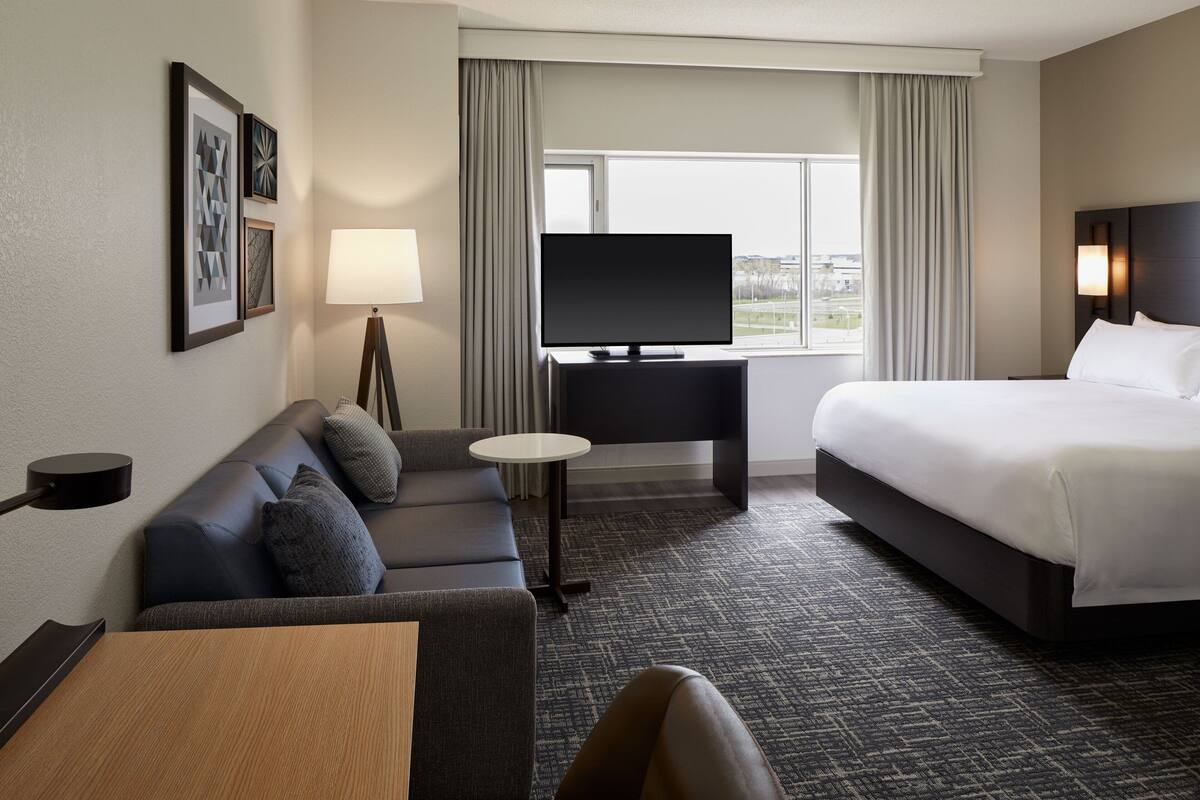 Een hotelkamer met een bed, een bank, een televisie, een lamp en een raam.