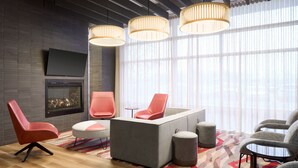 Een moderne woonkamer met een open haard, rode en grijze stoelen, een grijze bank en een kamerbreed tapijt met een patroon.