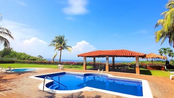 Uma piscina com deck ladrilhado, área de estar coberta e vista para o oceano.