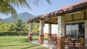 Un patio techado con mesa y sillas, vistas a una montaña y palmeras.