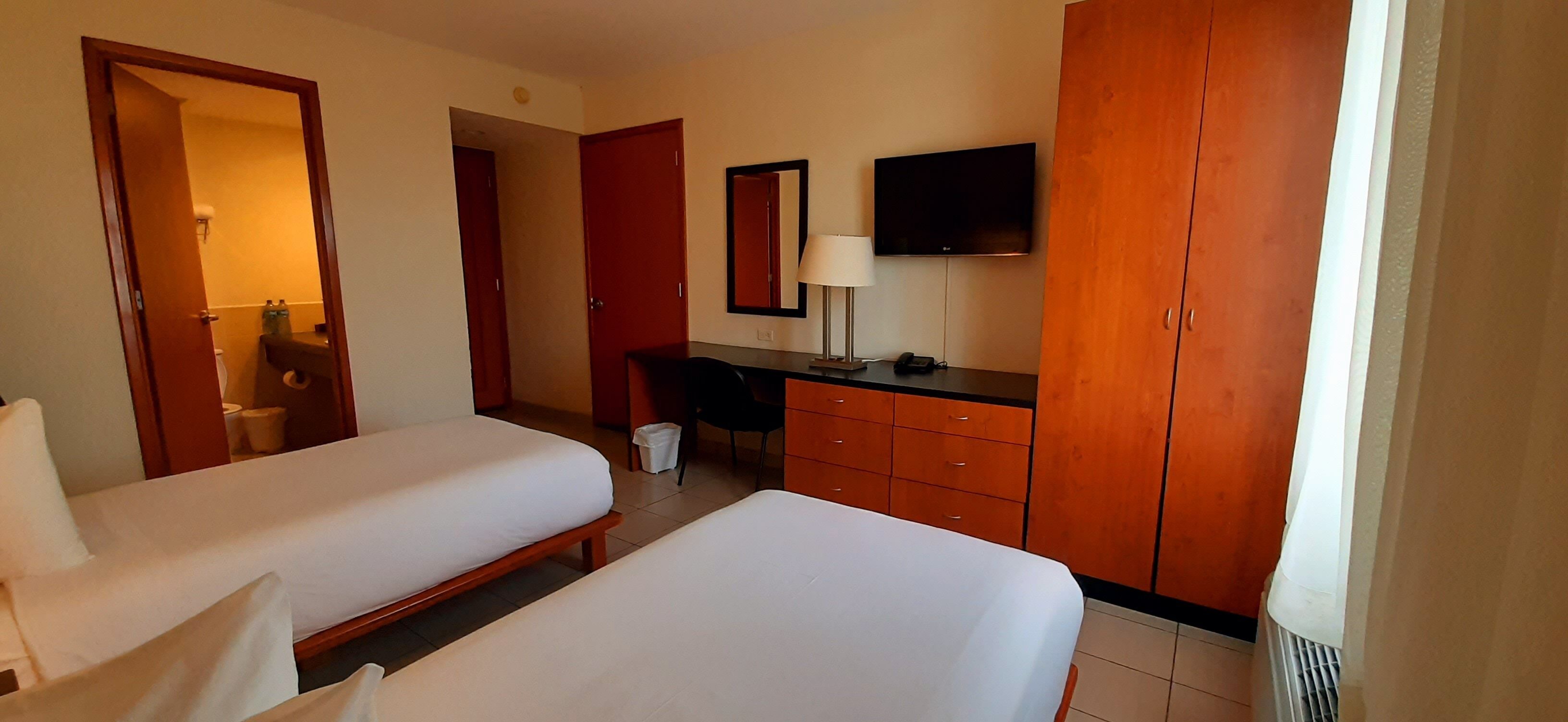 Une chambre d’hôtel avec deux lits, un bureau, une chaise, une télévision et une armoire.