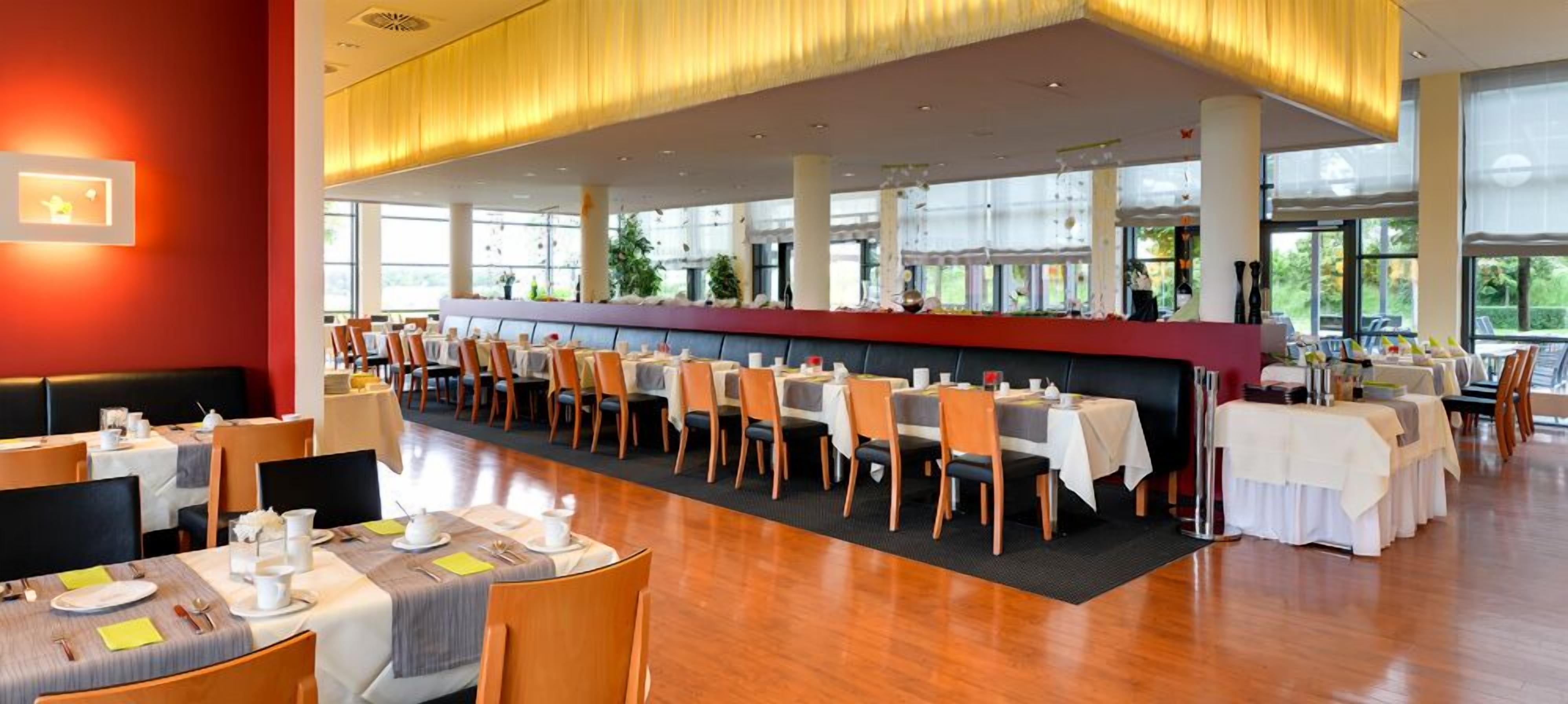 Un restaurante espacioso con techos altos, ventanas amplias y una larga barra con mesas y sillas.