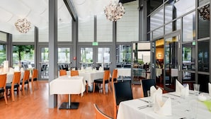 A restaurant with multiple tables and chairs, large windows, and hanging light fixtures.