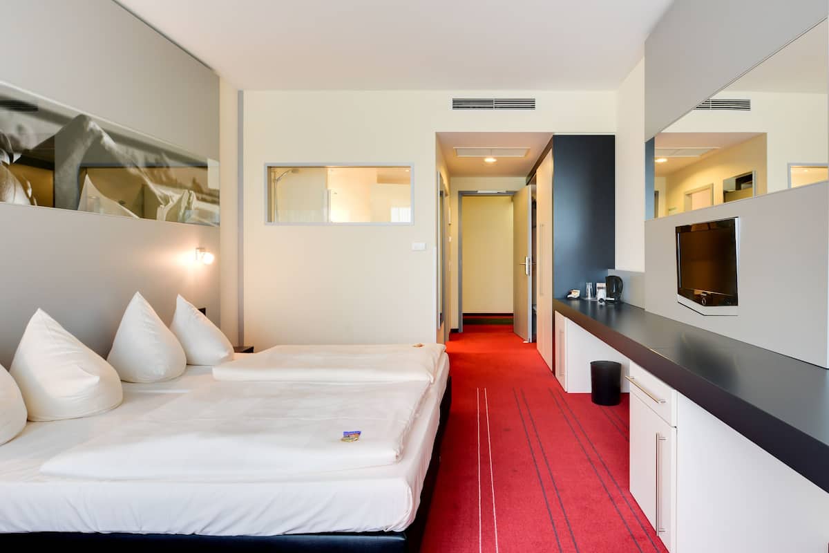 Een hotelkamer met een groot bed, een rode gang met vloerbedekking, een kitchenette en een spiegel aan de muur.