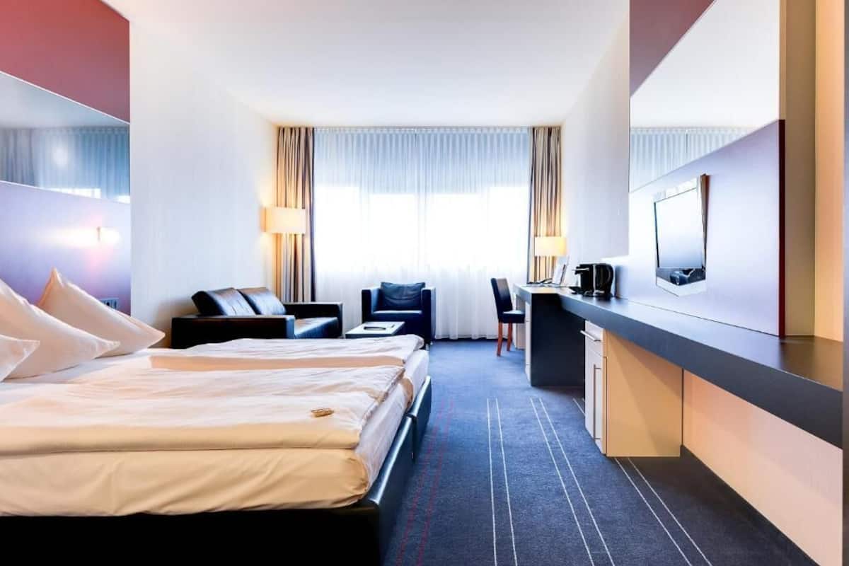 Een hotelkamer met twee bedden, een bureau, een stoel, een televisie en een minibar.