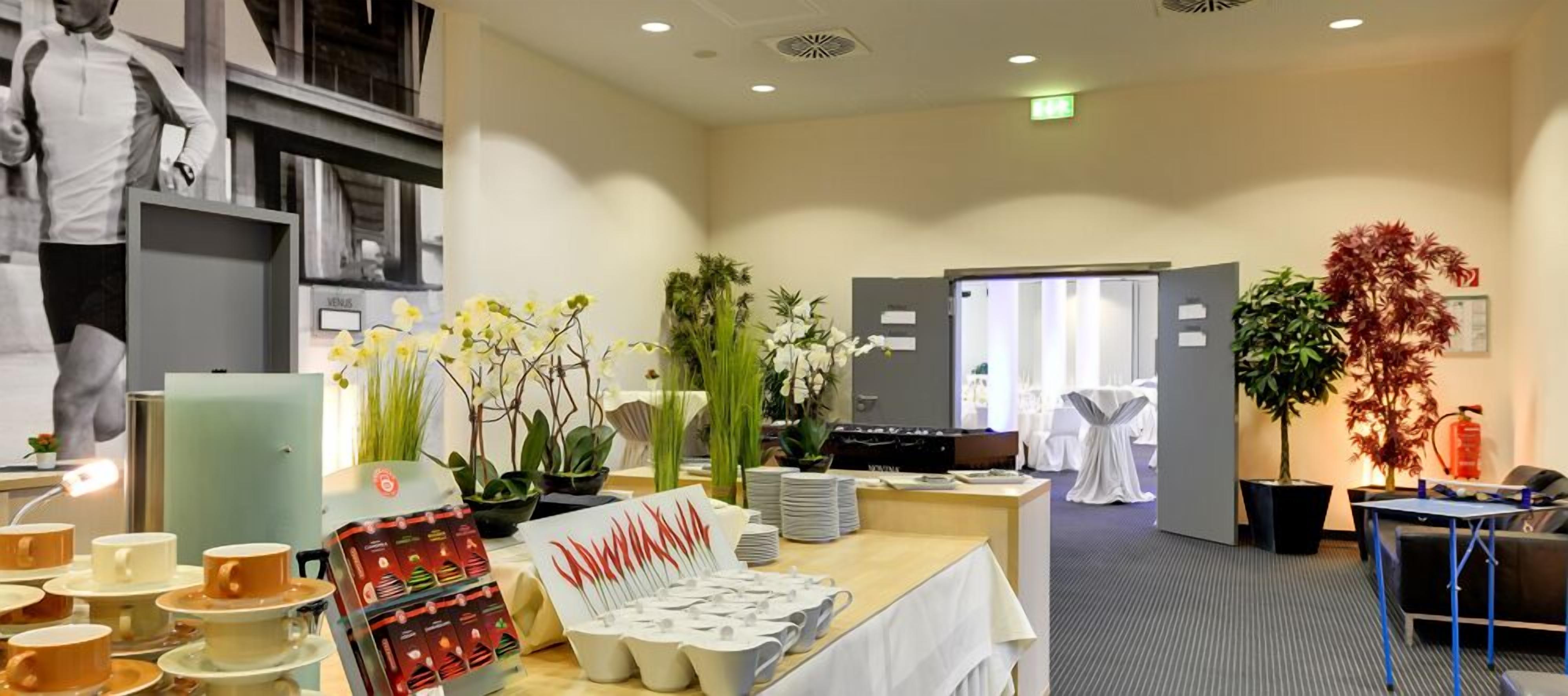 A hotel reception area with a reception desk, a white table with tea sets, and various potted plants.