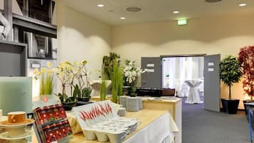 A hotel reception area with a reception desk, a white table with tea sets, and various potted plants.