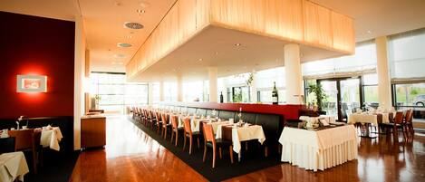 Un restaurante espacioso con una barra larga, techos altos y grandes ventanales.