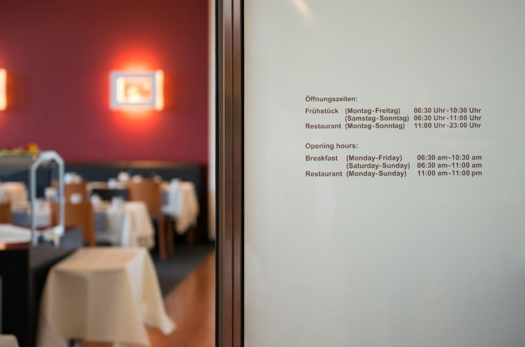 En restauranglokal med bord och stolar, och en meny på väggen som visar öppettiderna.