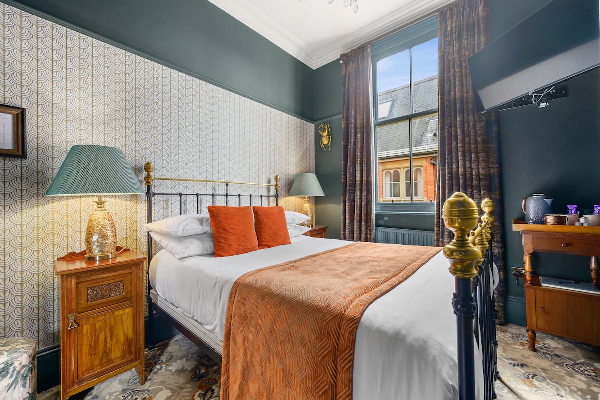 A hotel room with a bed, two nightstands, a dresser, and a window with curtains.