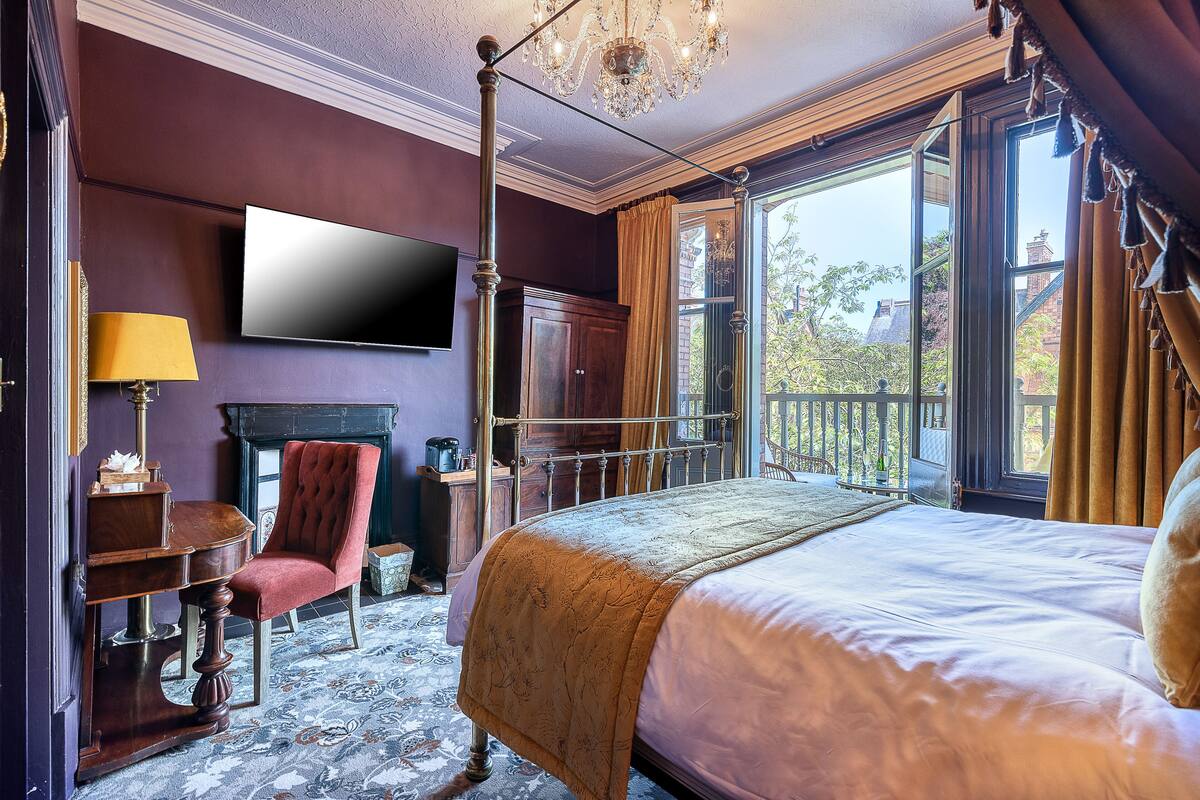 A bedroom with a large bed, a television, a chair, and a fireplace.