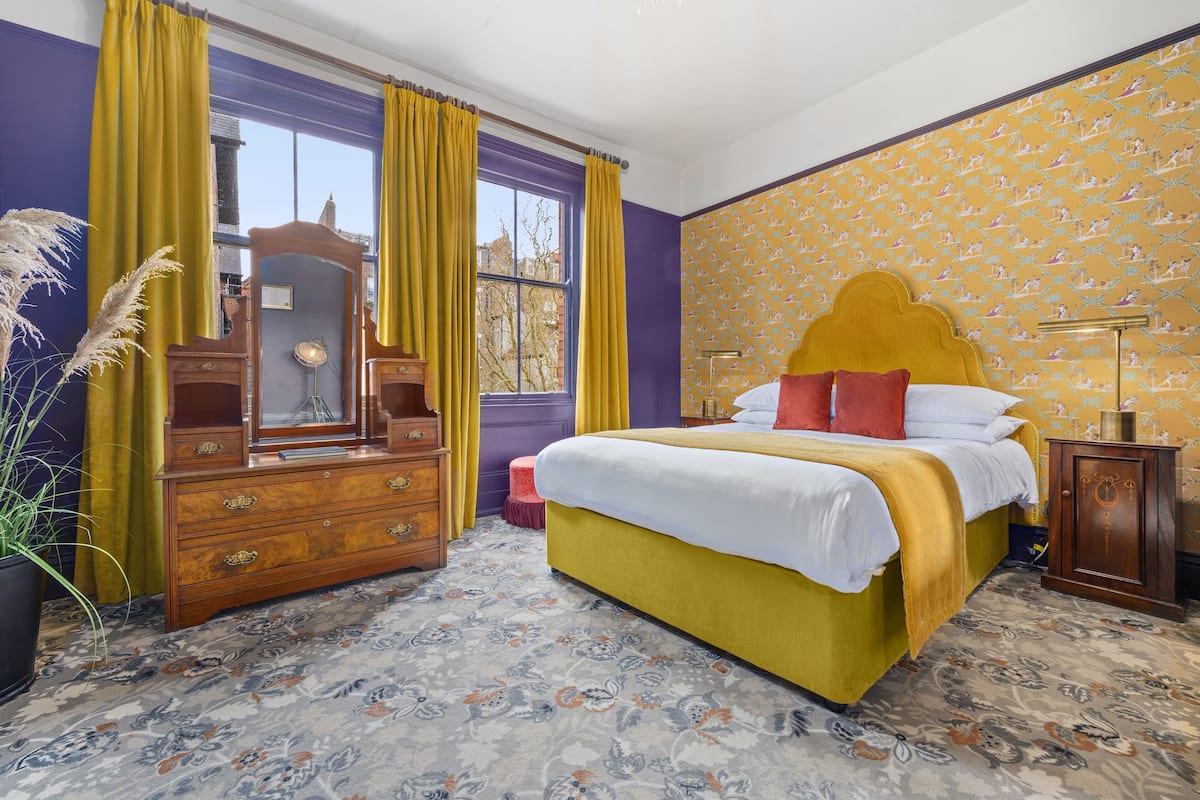 A bedroom with a large bed, a dresser, a mirror, and a window with curtains.