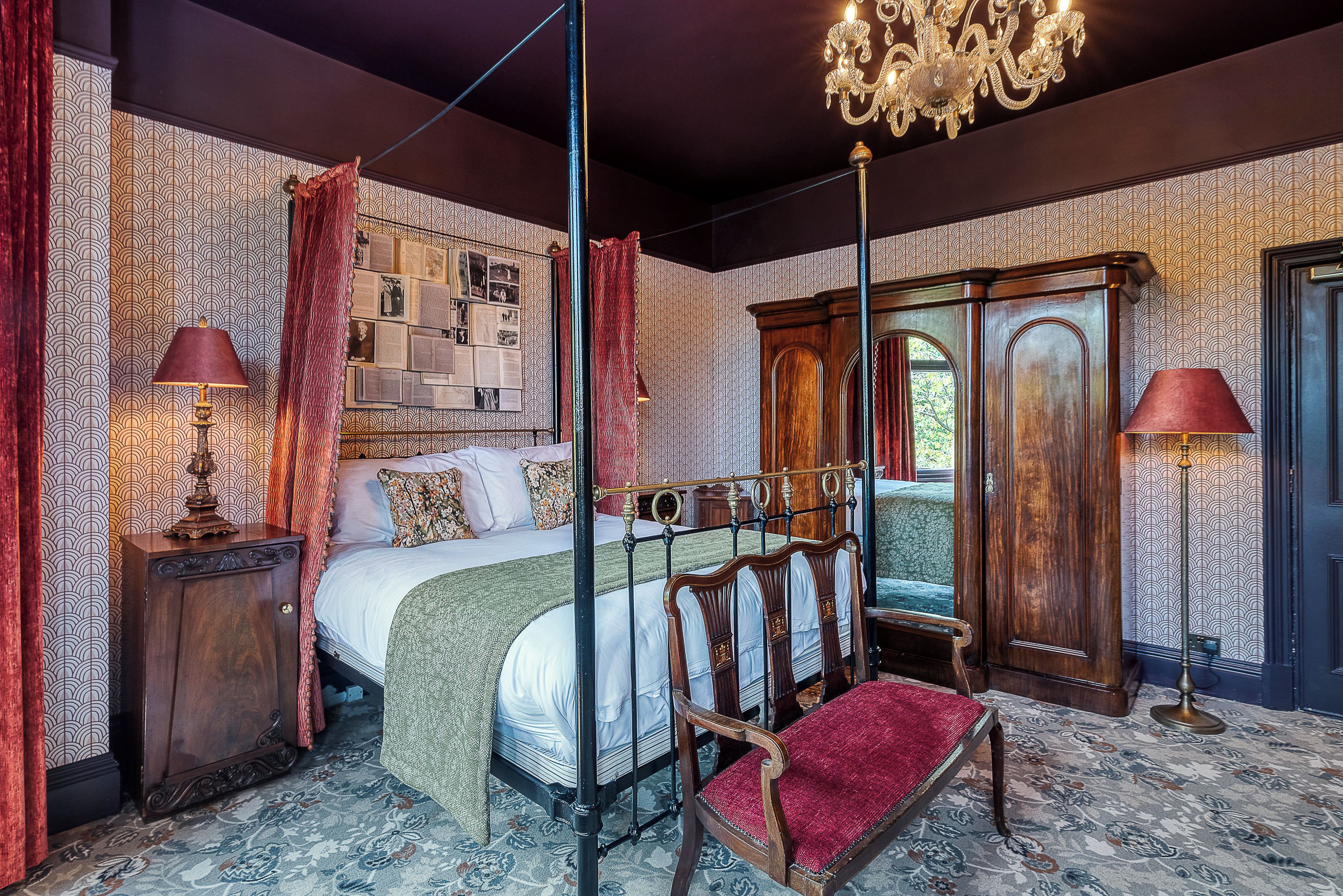 Een klassieke slaapkamer met een hemelbed, een kroonluchter en behang met een patroon.