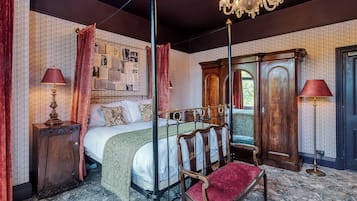 Ein klassisches Schlafzimmer mit einem Himmelbett, einer Chandelüster und einer Wandtapete mit Muster.