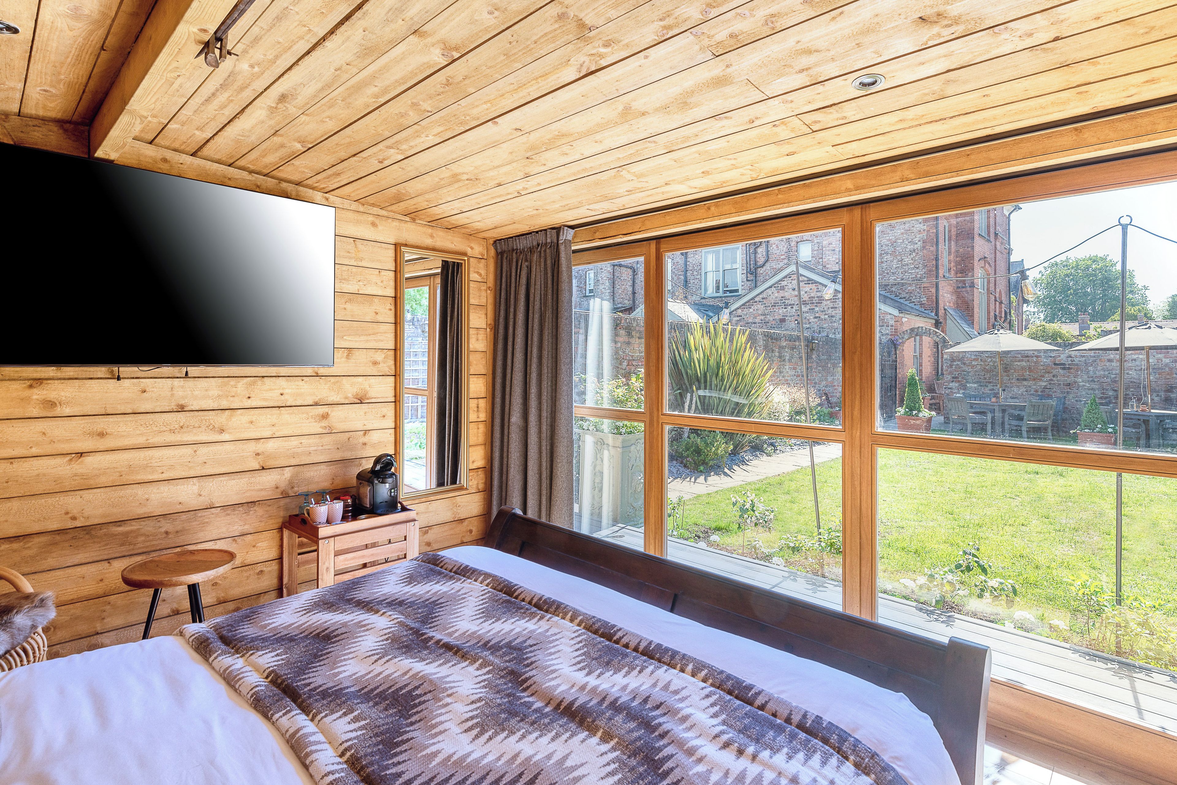 A bedroom with a large bed, wooden walls, a TV mounted on the wall, and a window with a view of the outside.