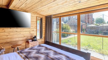 A bedroom with a large bed, wooden walls, a TV mounted on the wall, and a window with a view of the outside.
