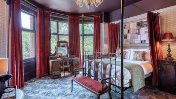 A room with a four-poster bed, a desk with a chair, a chandelier, and a large window with curtains.