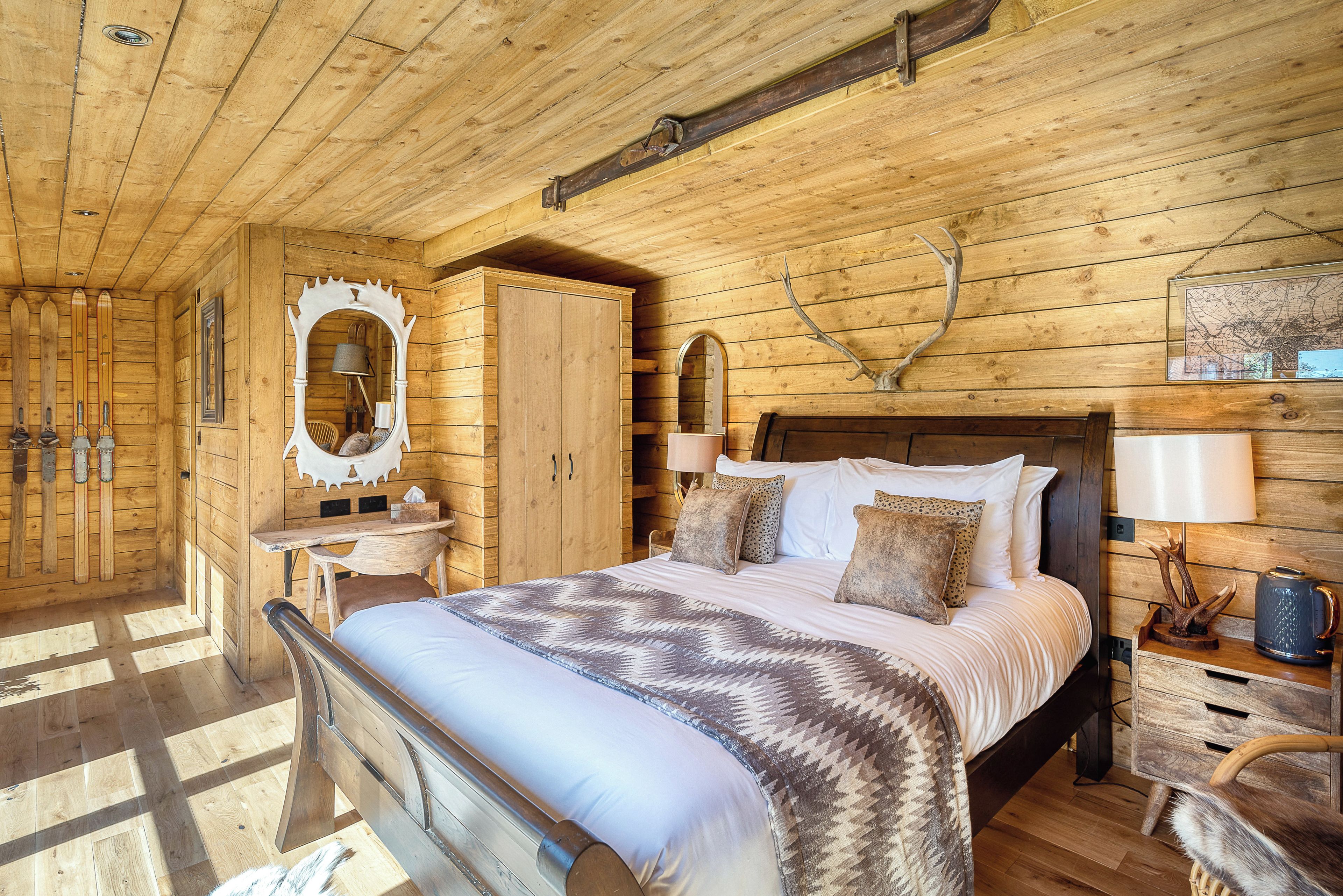Ein Holzblockhaus-Interieur mit einem Bett, einer Kommode, einem Spiegel und Skiern an der Wand.